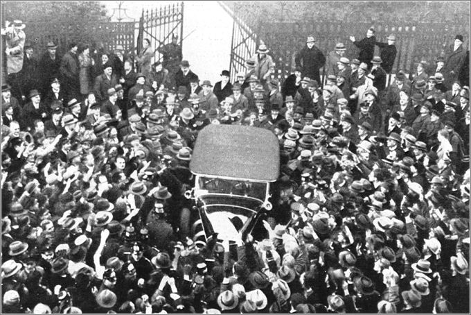 An automobile in which Adolf Hitler is riding moves through a crowd of supporters as it leaves the Chancellery